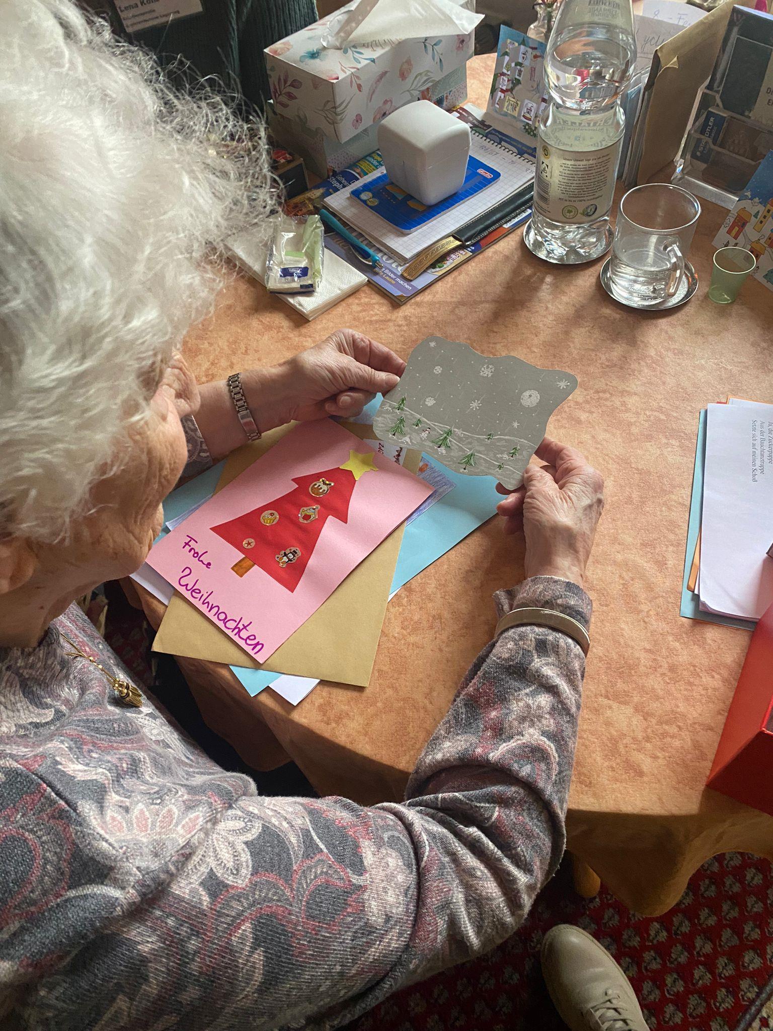 Eine Seniorin sitzt am Tisch und betrachtet ihre Weihnachtskarten