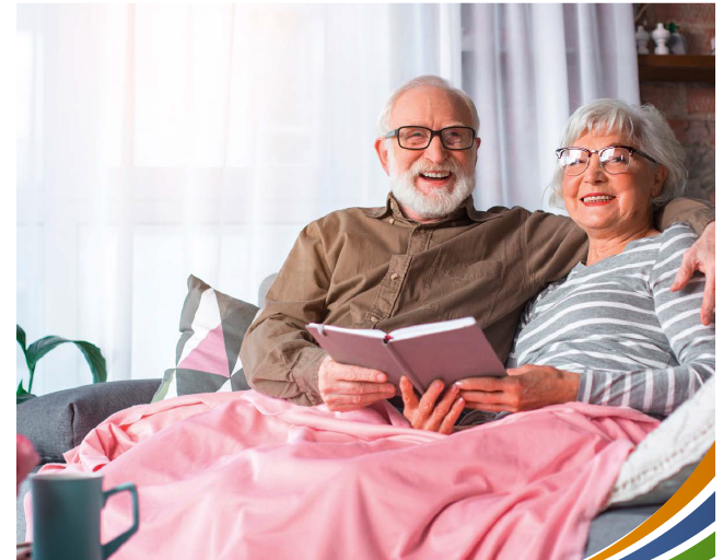 Ein älteres Ehepaar sitzt mit einer rosa Decke auf dem Sofa und liest