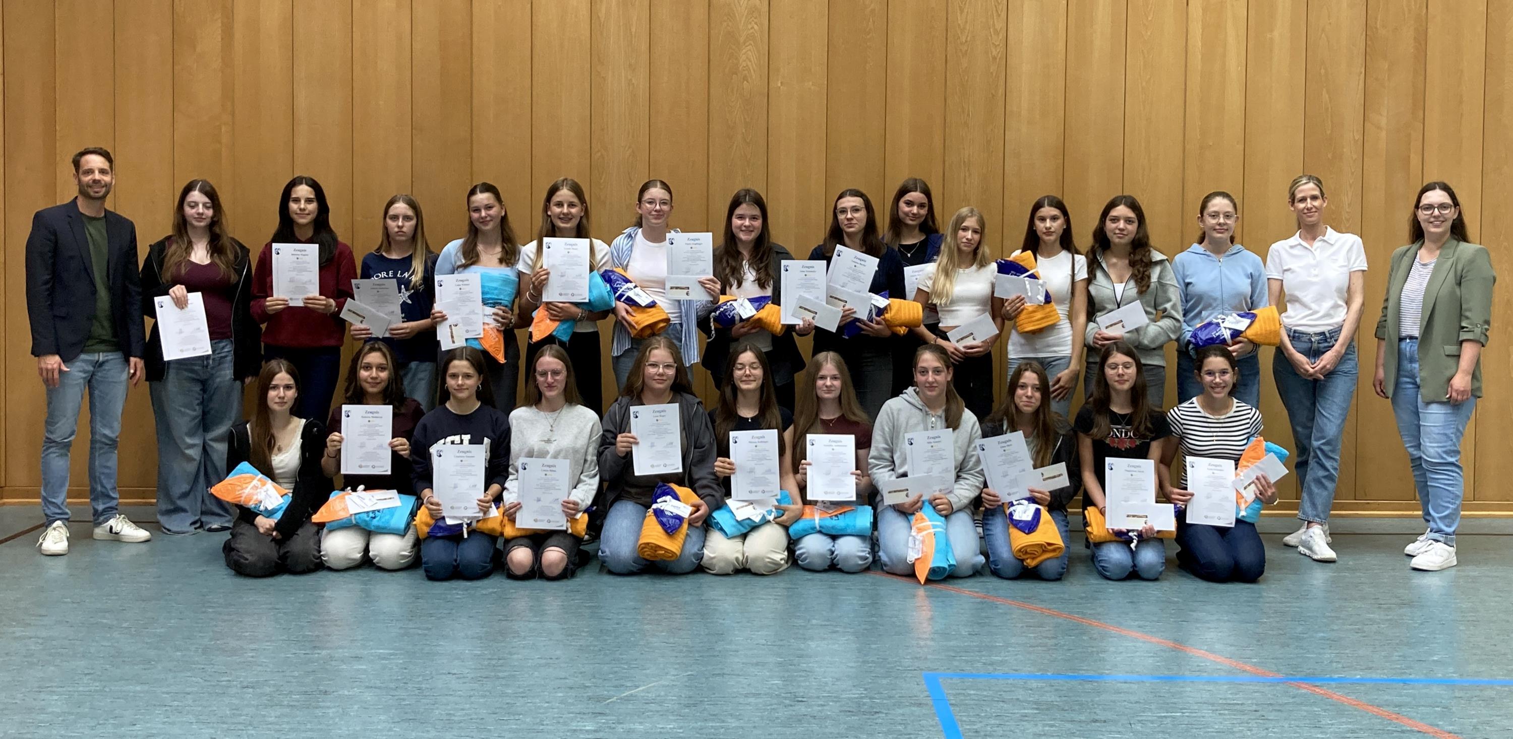 26 Schülerinnen halten in der Turnhalle ein Zertifikat in die Kamera