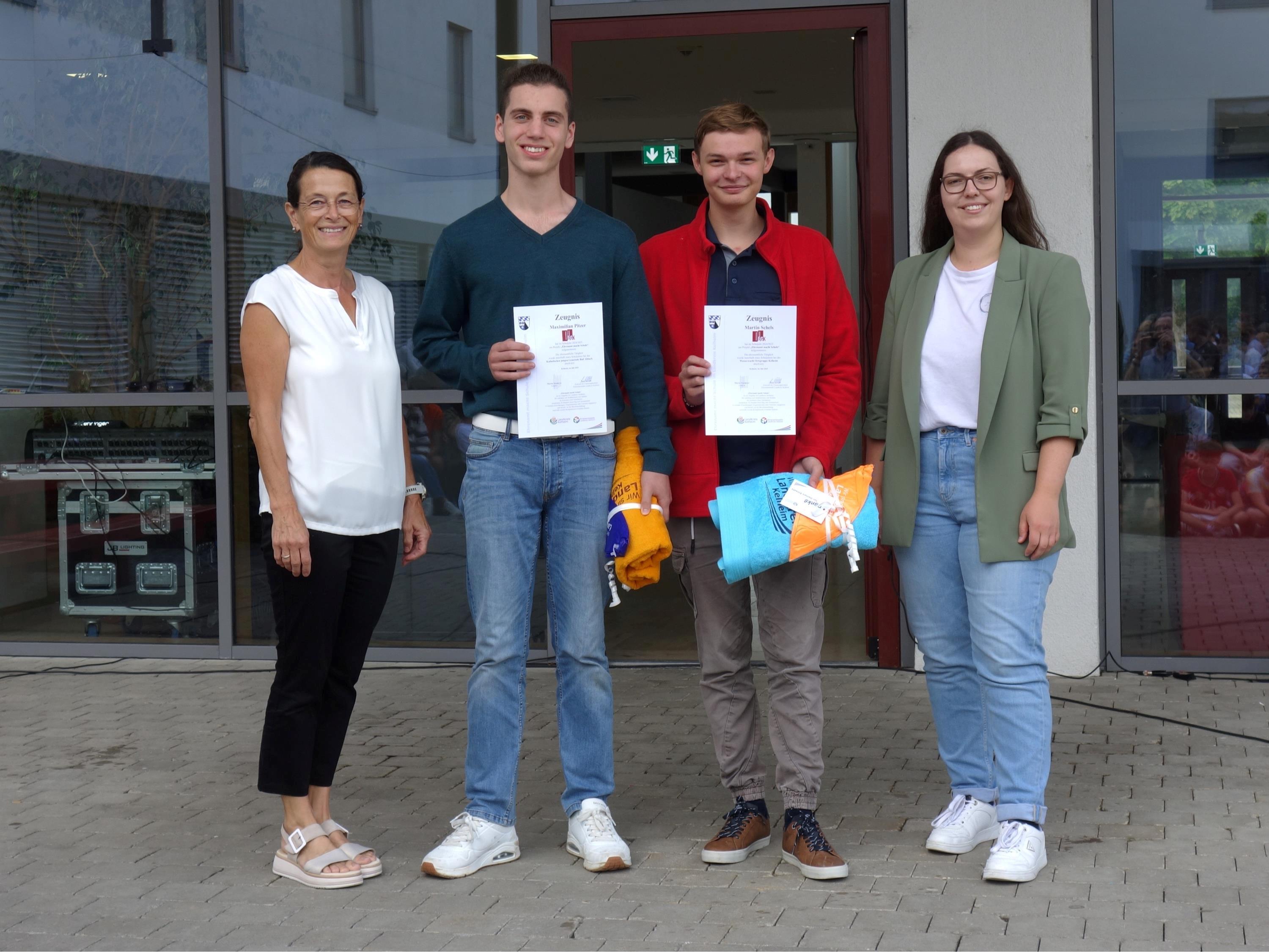 Vor dem Schuleingang präsentieren zwei Schüler ihre Zertifikate
