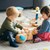 2 Kleinkinder sitzen am Boden, spielen gemeinsam mit einem Stofftier