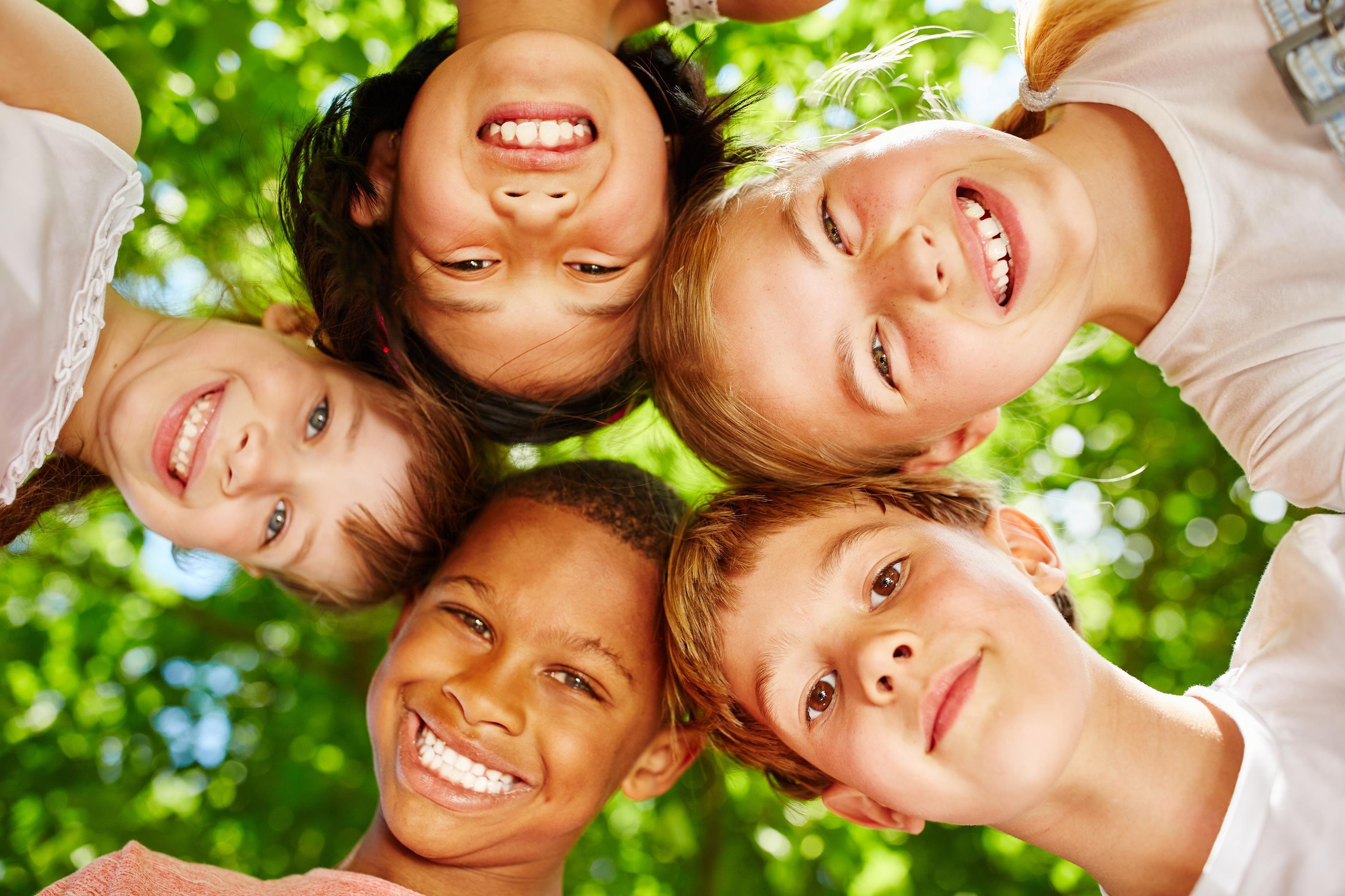 Fünf Kinder schauen lächelnd und Kopf an Kopf stehend nach unten