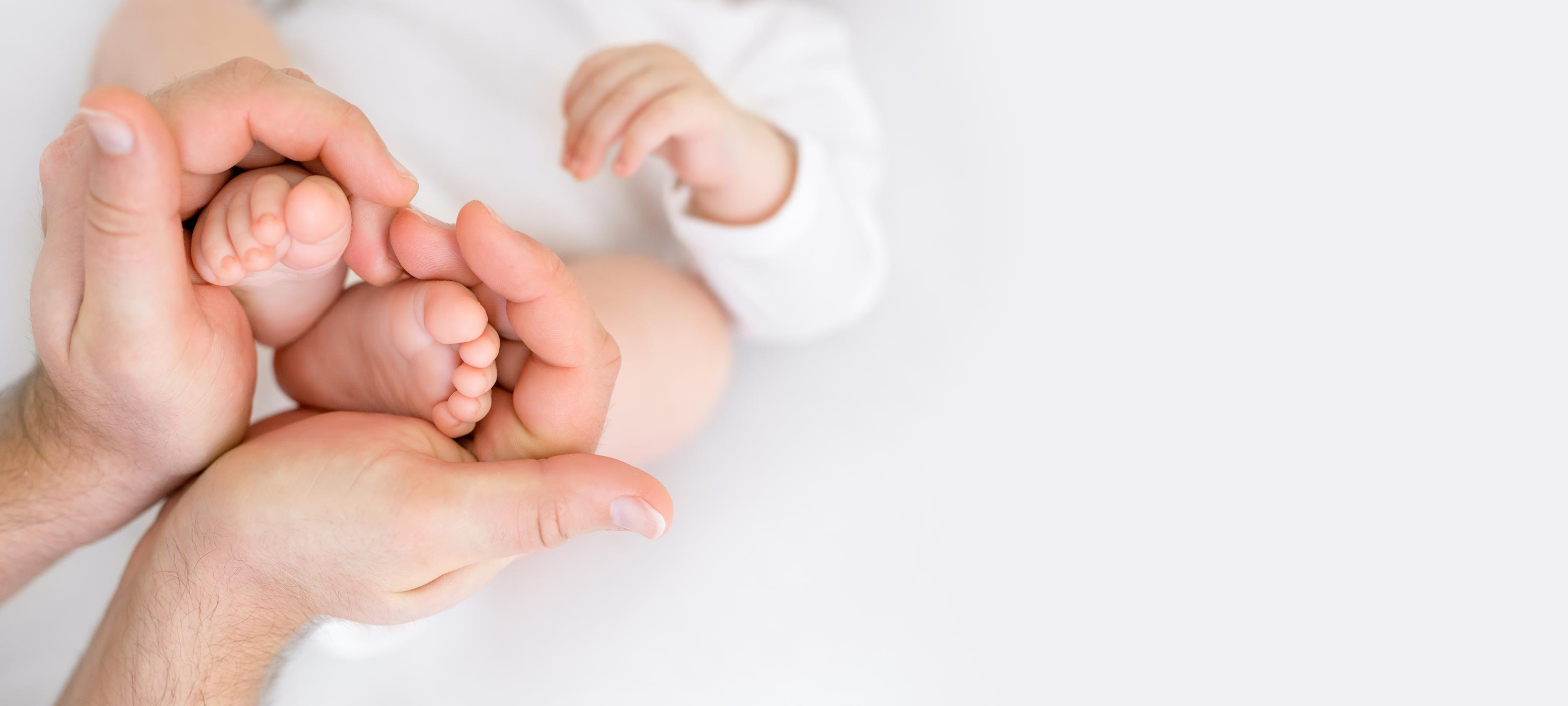 Zu einem Herz geformte Hände einer Frau, die Babyfüße festhält