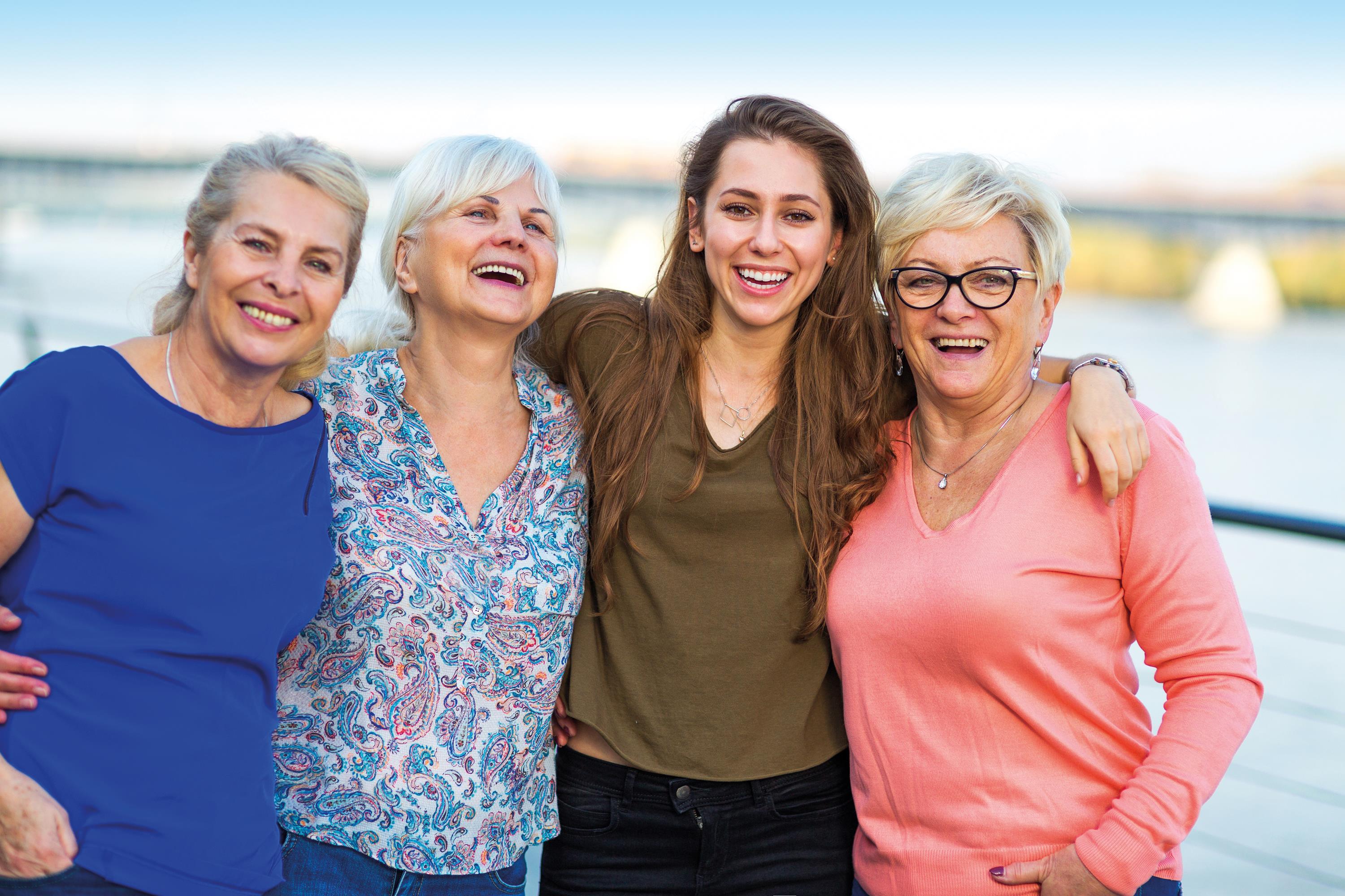 Eine junge und drei ältere Frauen lachen Arm in Arm in die Kamera