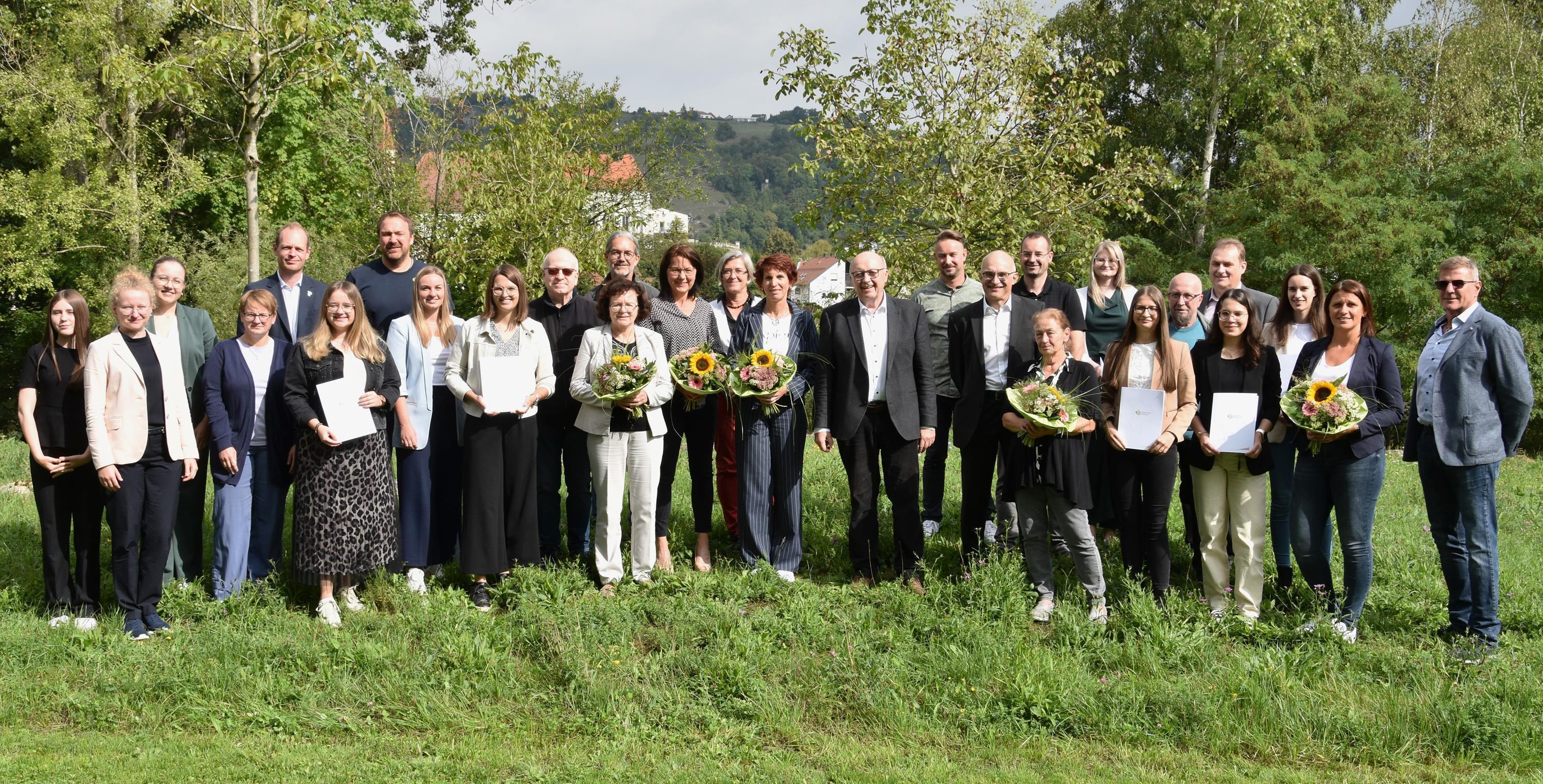 Zwölf geehrte Mitarbeiter mit Kollegen und dem Landrat auf einer Wiese