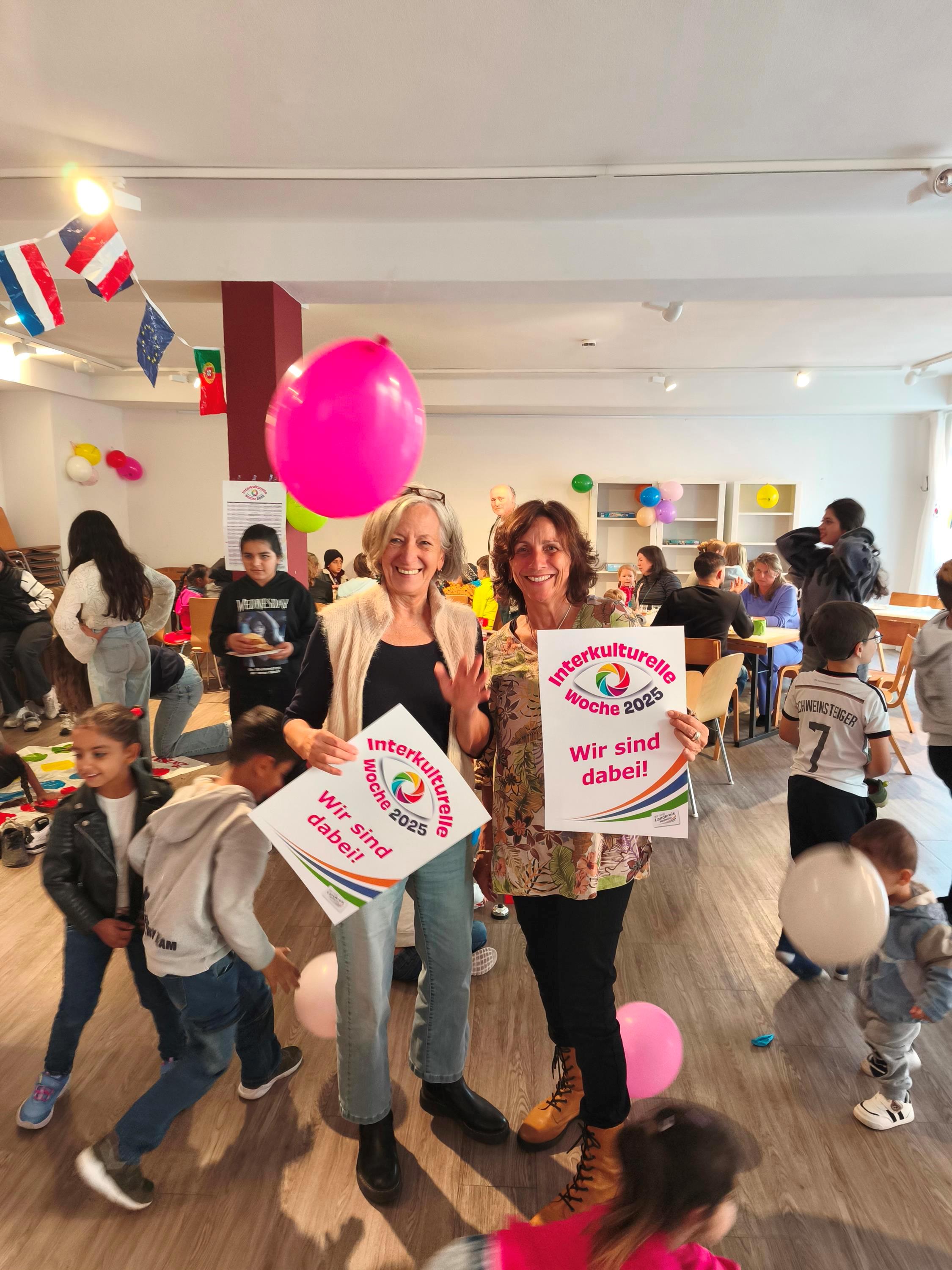 interkultureller Spielenachmittag Zwei Frauen halten in Mitten von spielenden Kindern Plakate hoch