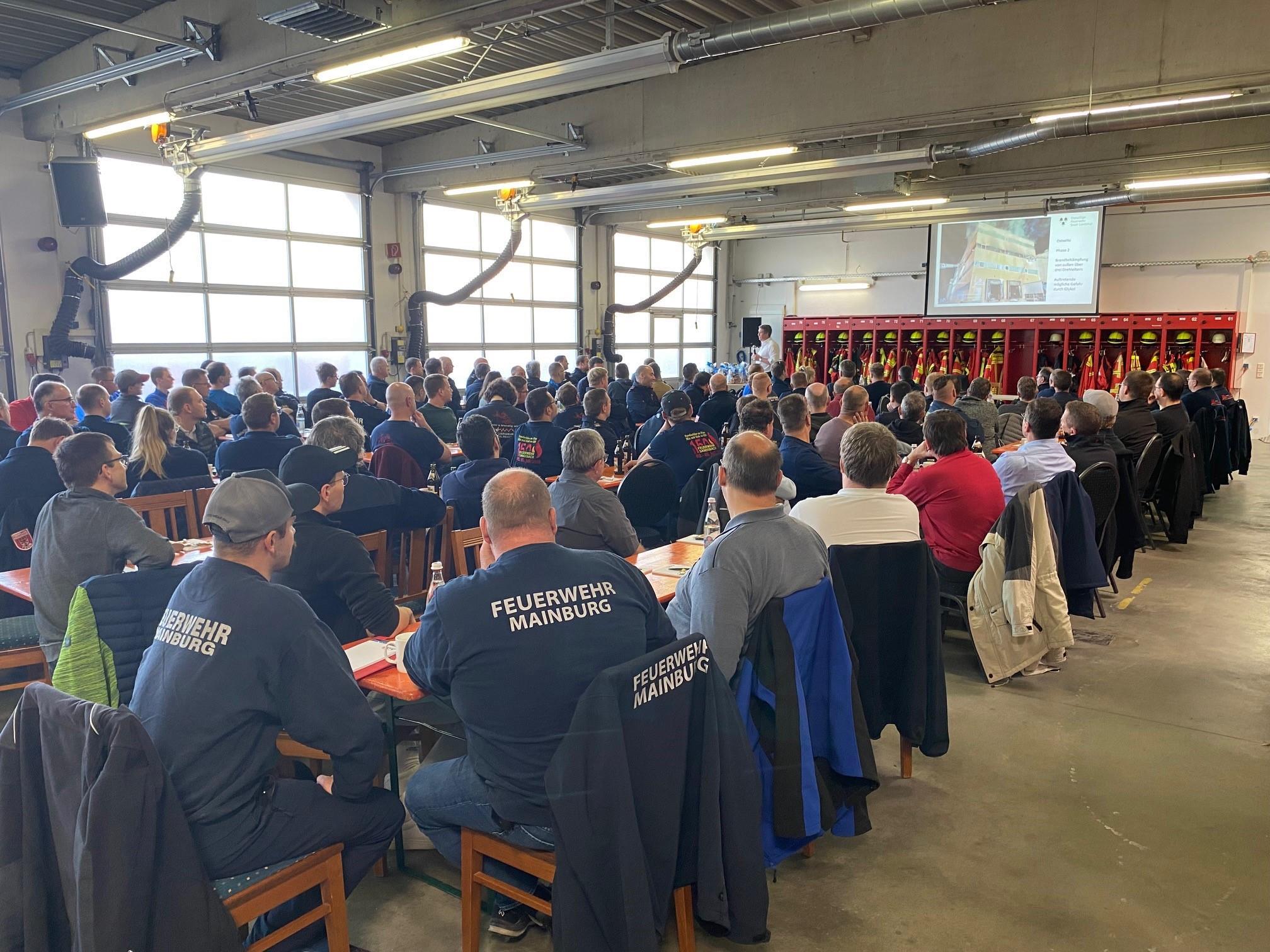 Feuerwehrler hören im Feuerwehrhaus bei einem Vortrag zu.