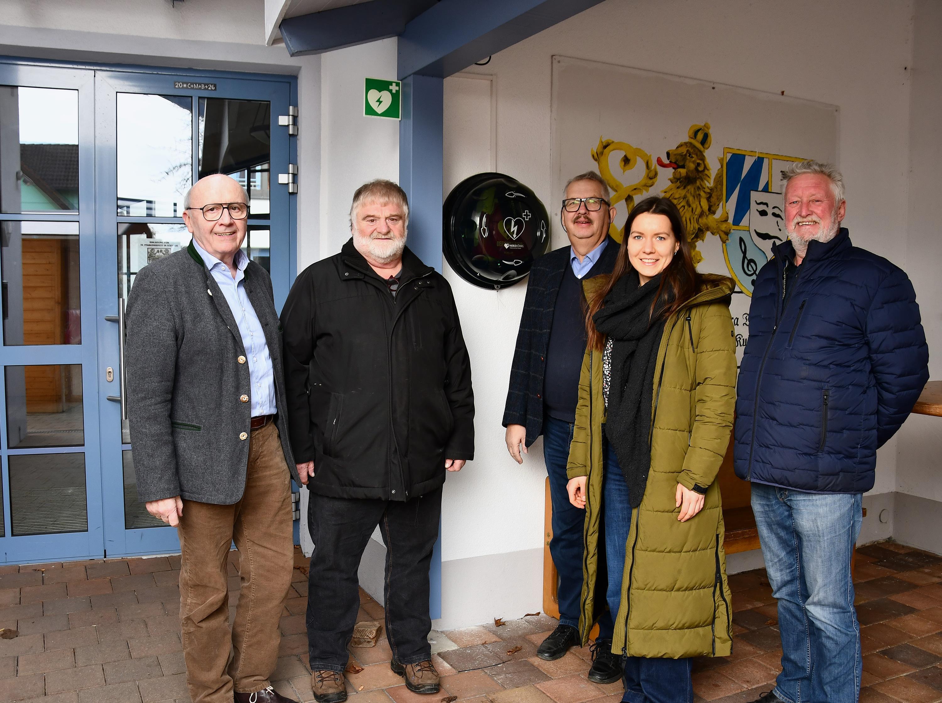 Fünf Personen mit Blick Richtung Kamera stehen neben dem Defibrillator