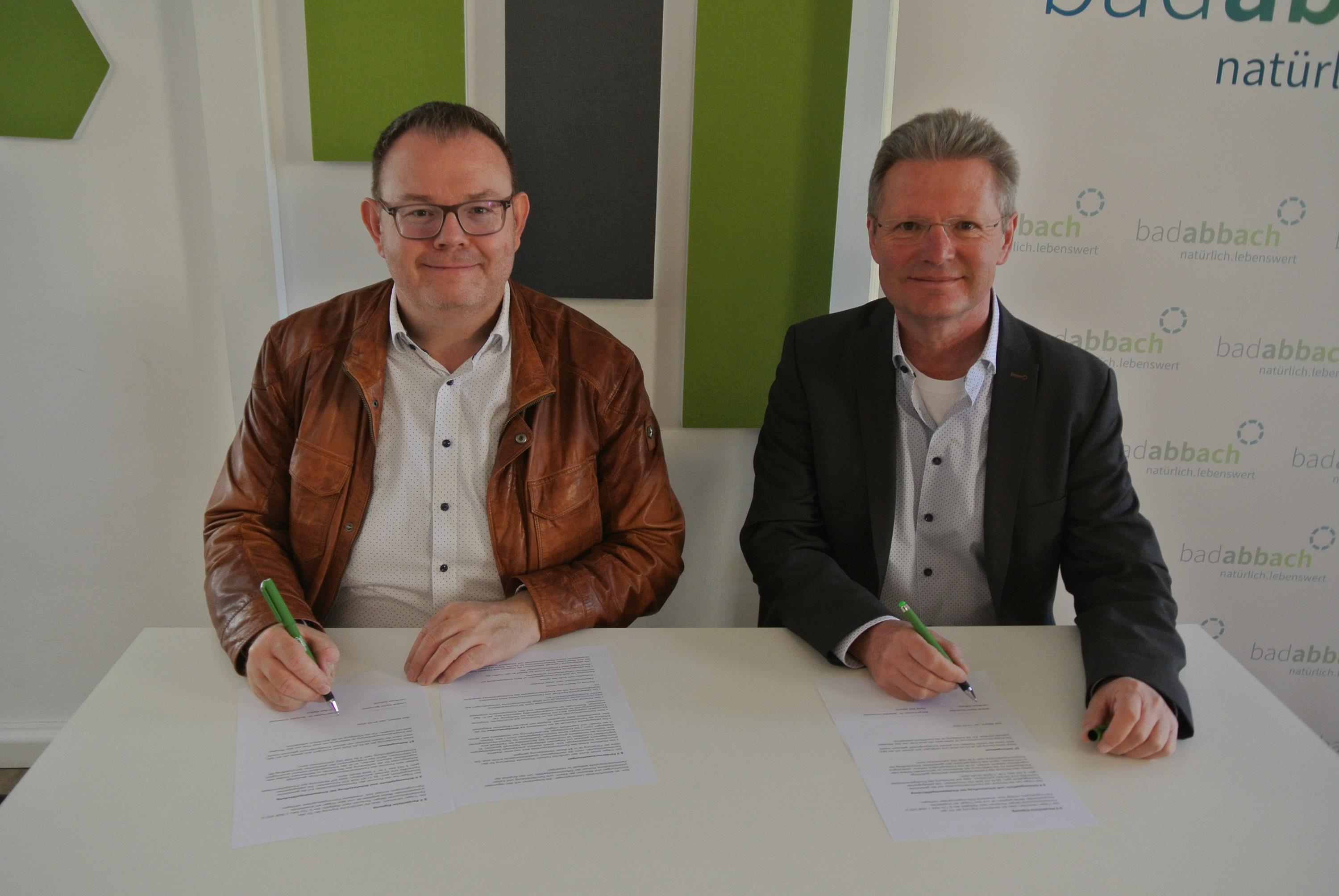 Zwei Männer sitzen an einem Tisch und unterschreiben den Vertrag.