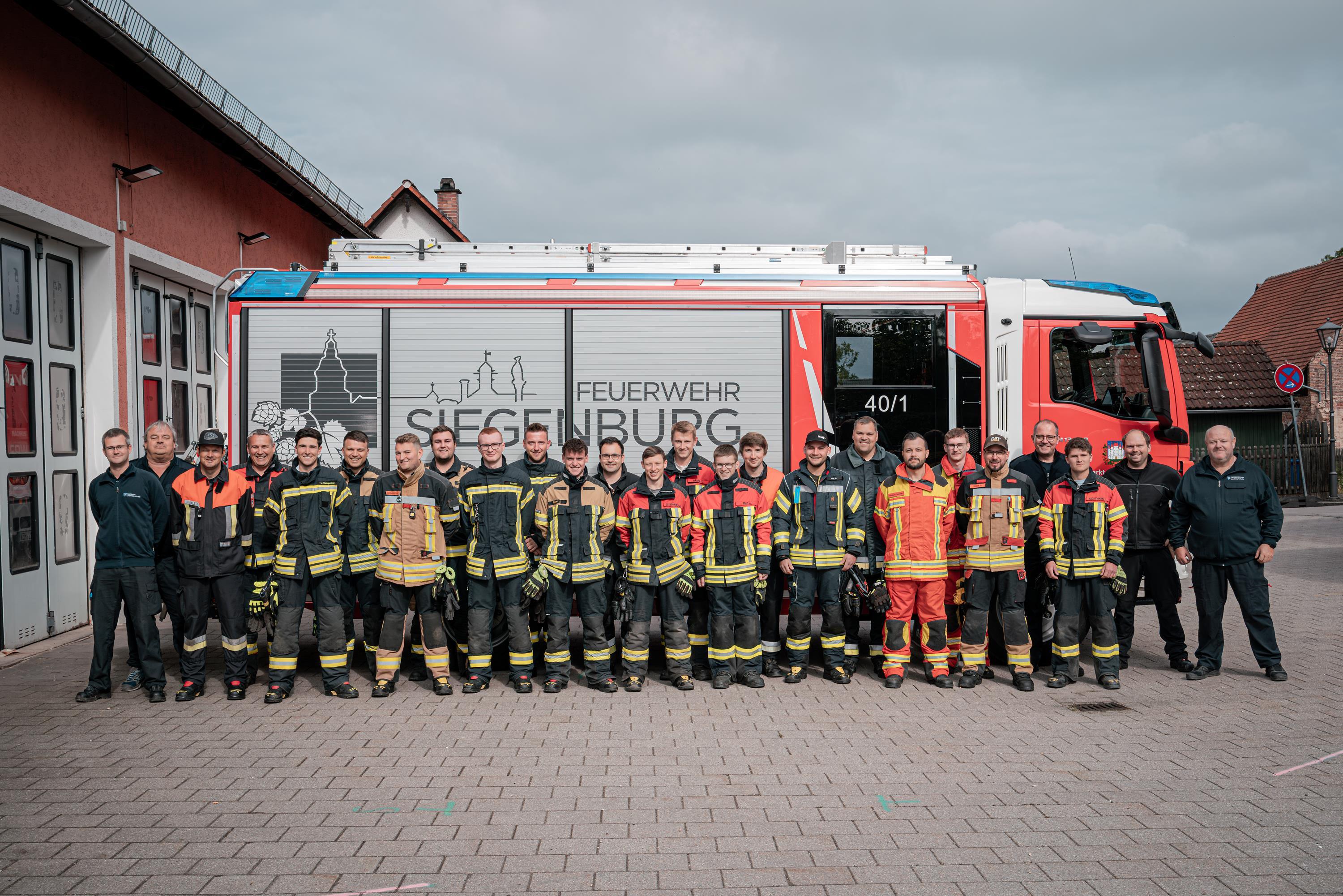 25 Feuerwehrmänner vor einem Feuerwehrauto