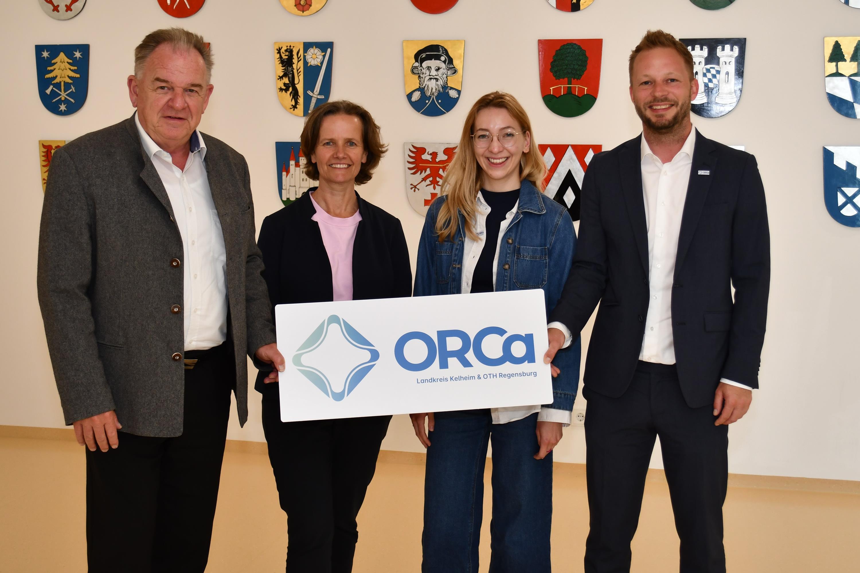 Zwei Männer flankieren zwei Frauen und halten Schild mit ORCa