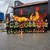 16 Feuerwehrmänner vor Flammen und einem schwarzen Container