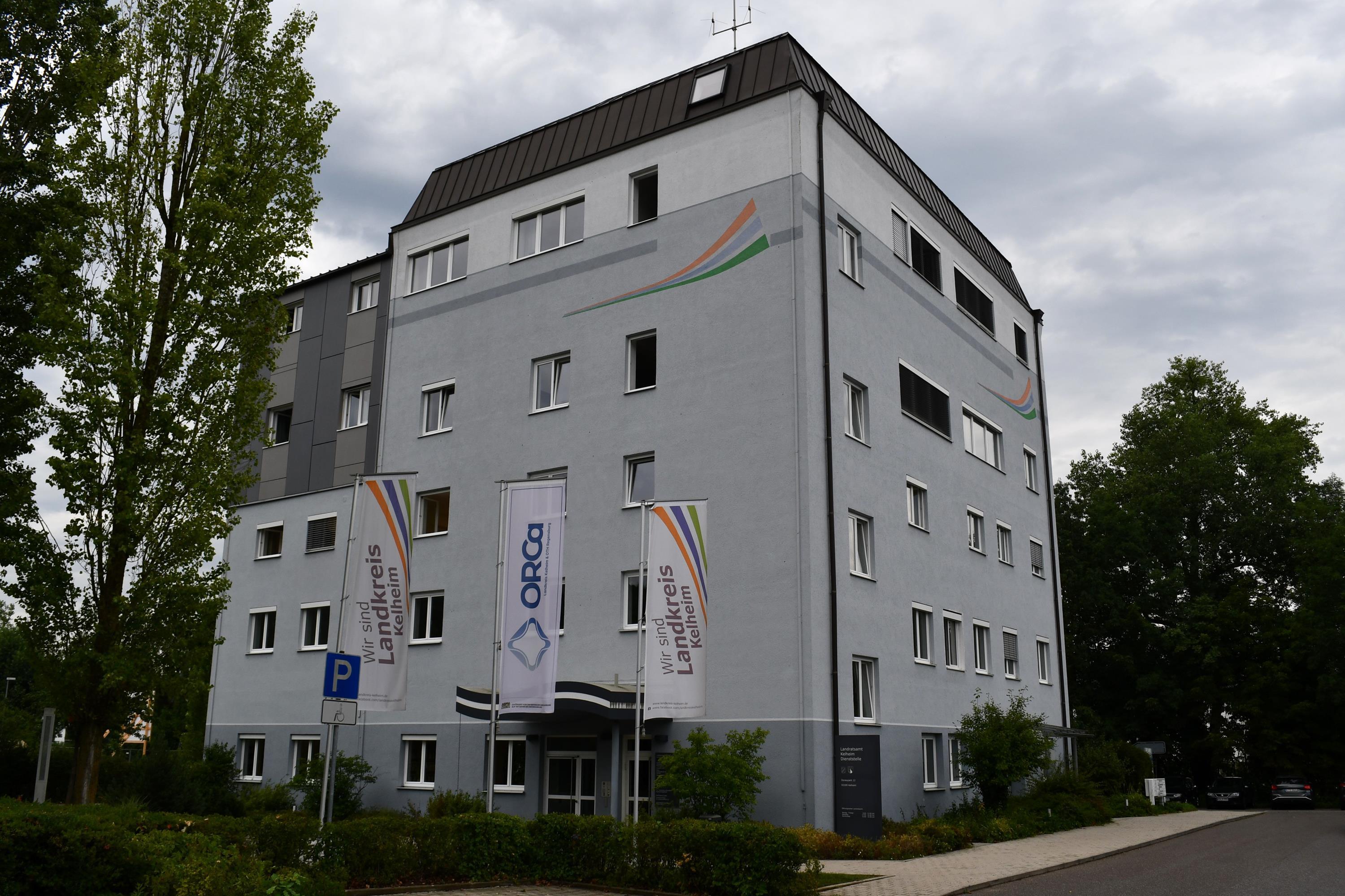 Fünfstöckiges graues Gebäude mit Landkreis-Fahnen davor