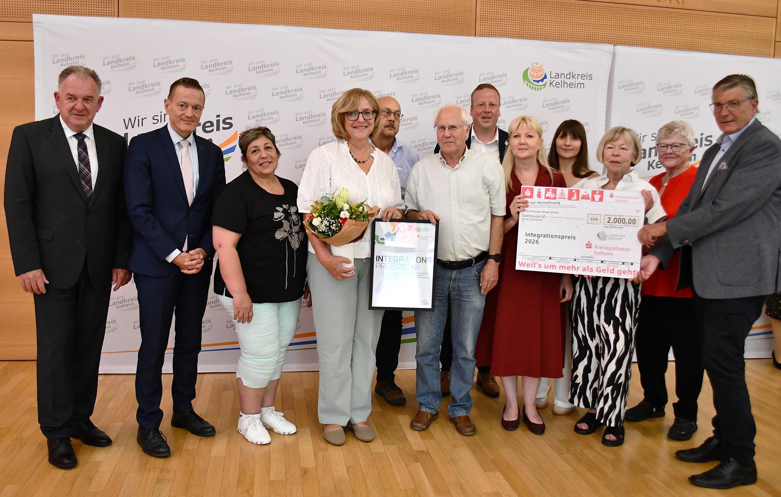 12 Personen zu sehen, 2 mit Urkunde und Blumen, 3 mit Geldscheck