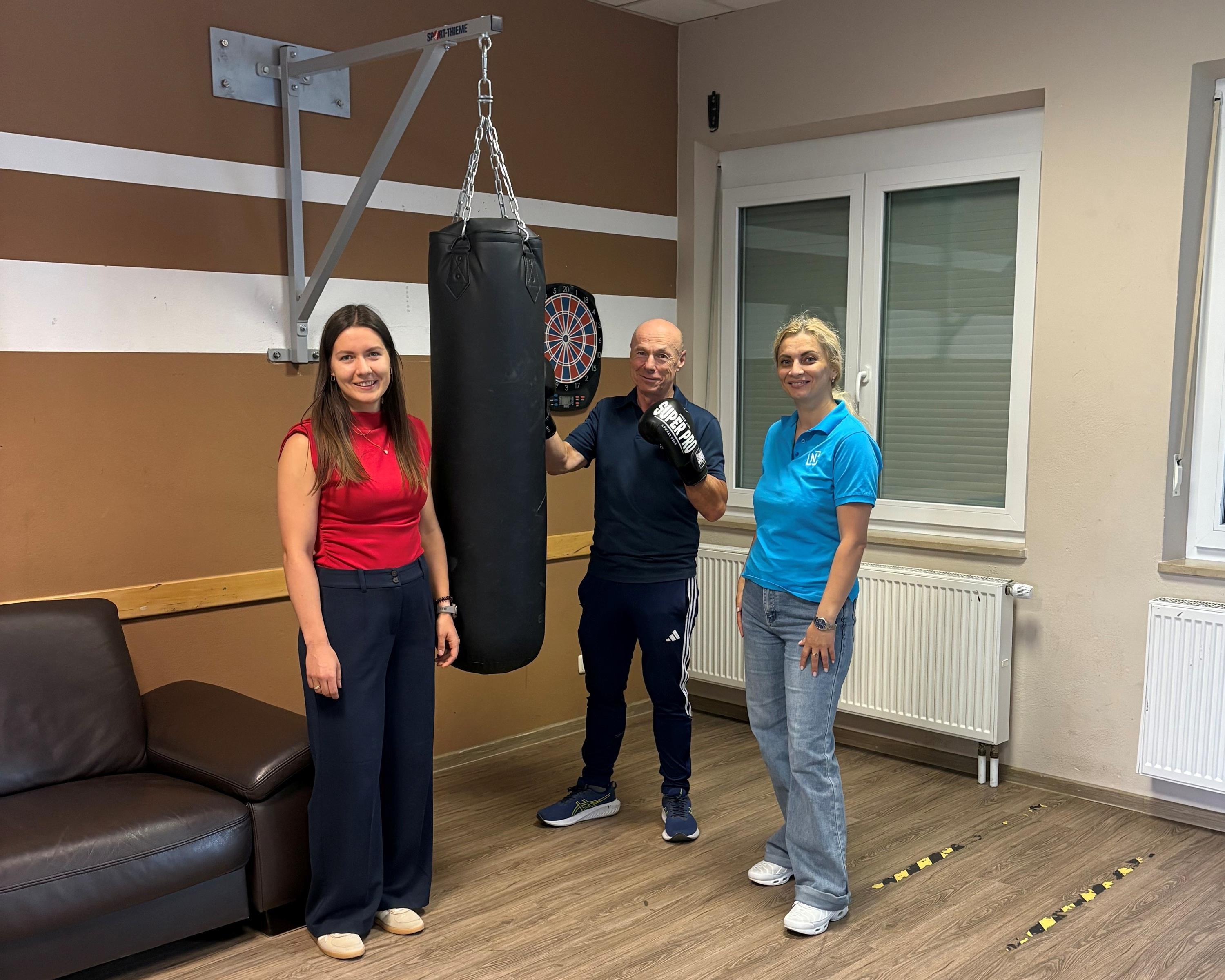 Zwei Frauen und ein Mann mit Boxhandschuhen flankieren einen Boxsack