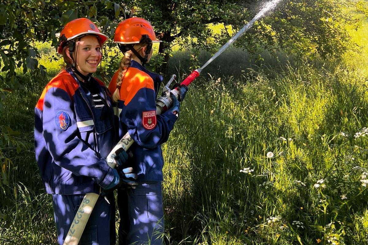 Zwei Jugendliche halten einen Schlauch, aus dem Wasser spritzt