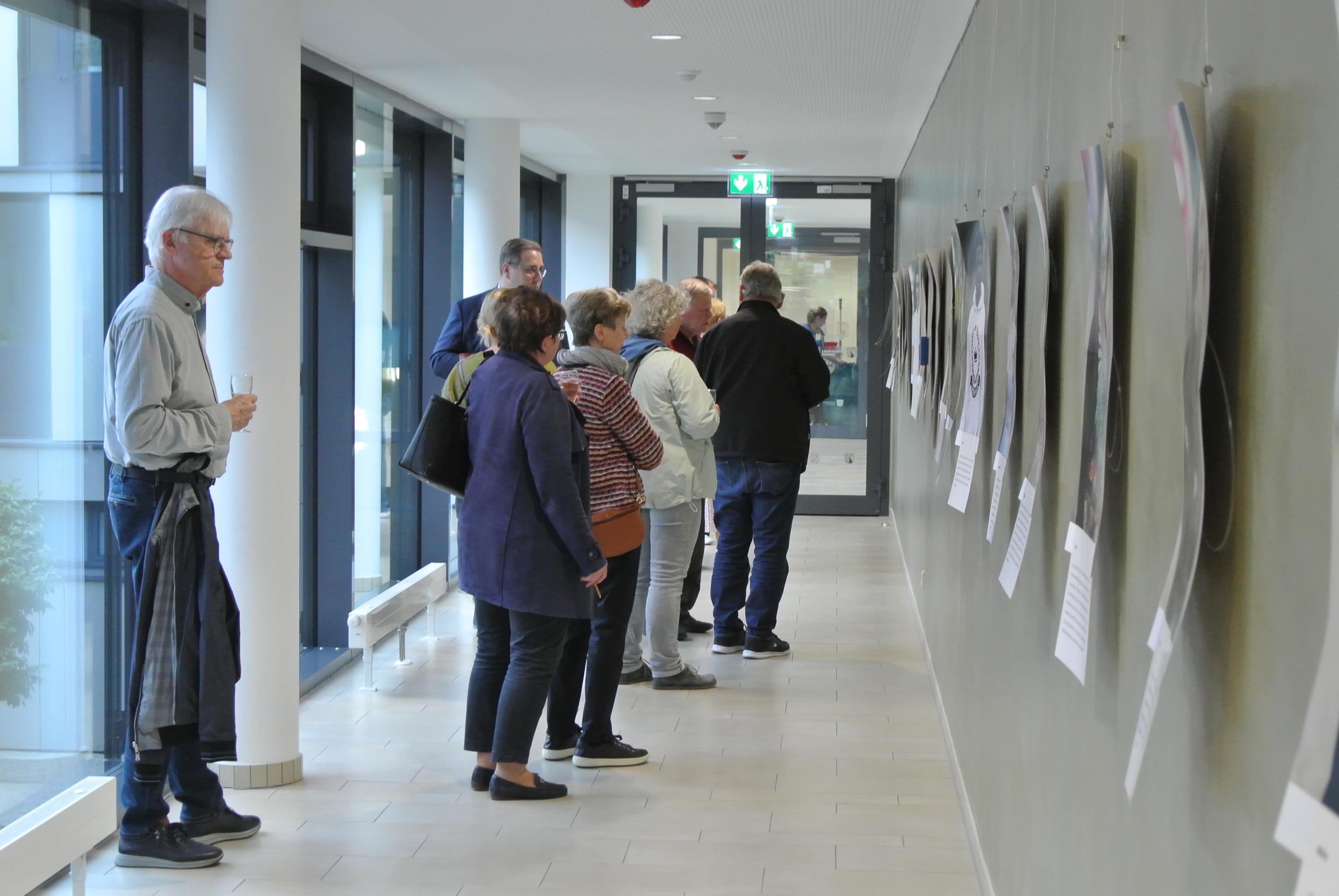 Mehrere Menschen sehen sich an einer Wand aufgehängte Bilder an