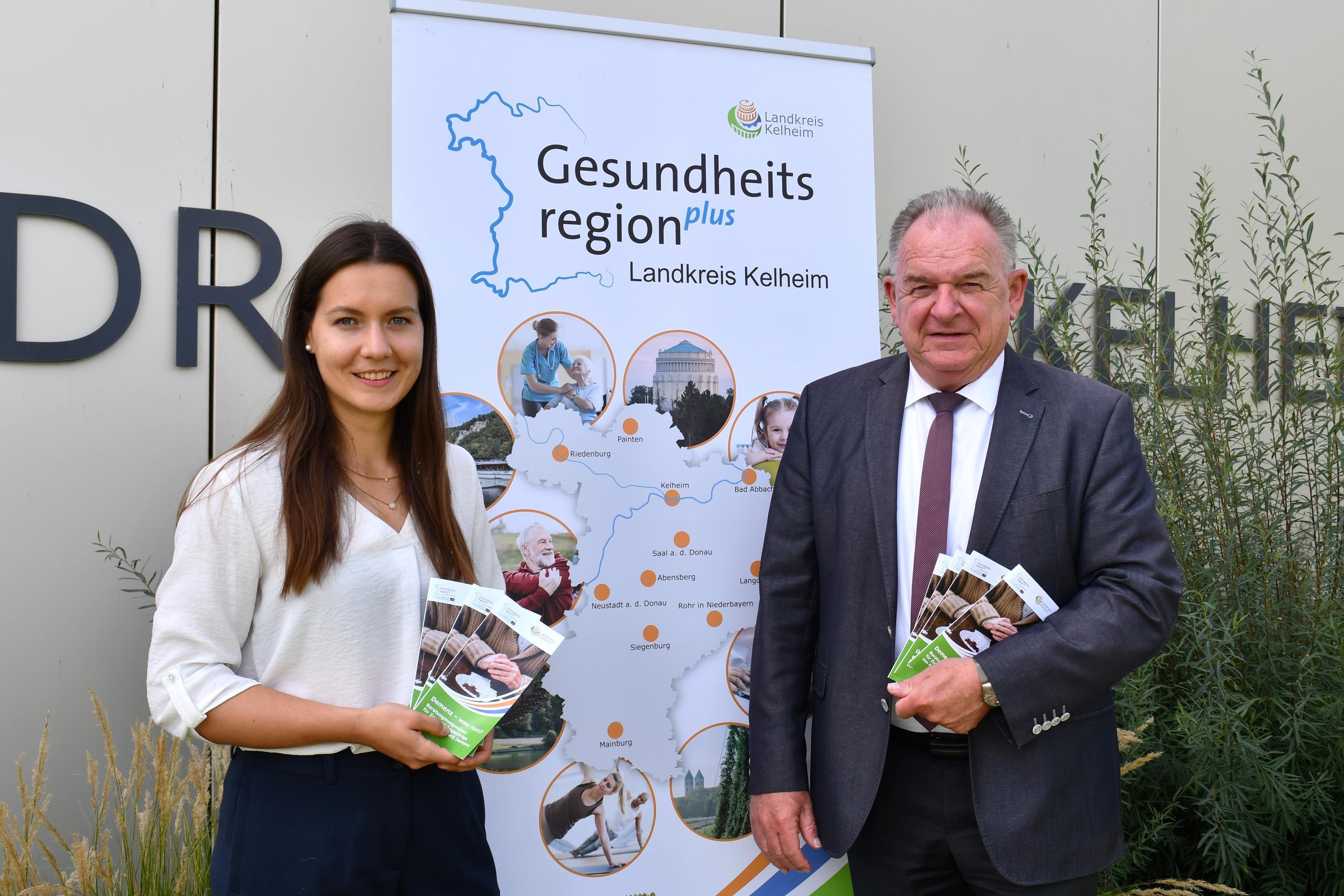 Frau und Mann stehen vor dem Landratsamt und halten kleine Broschüren