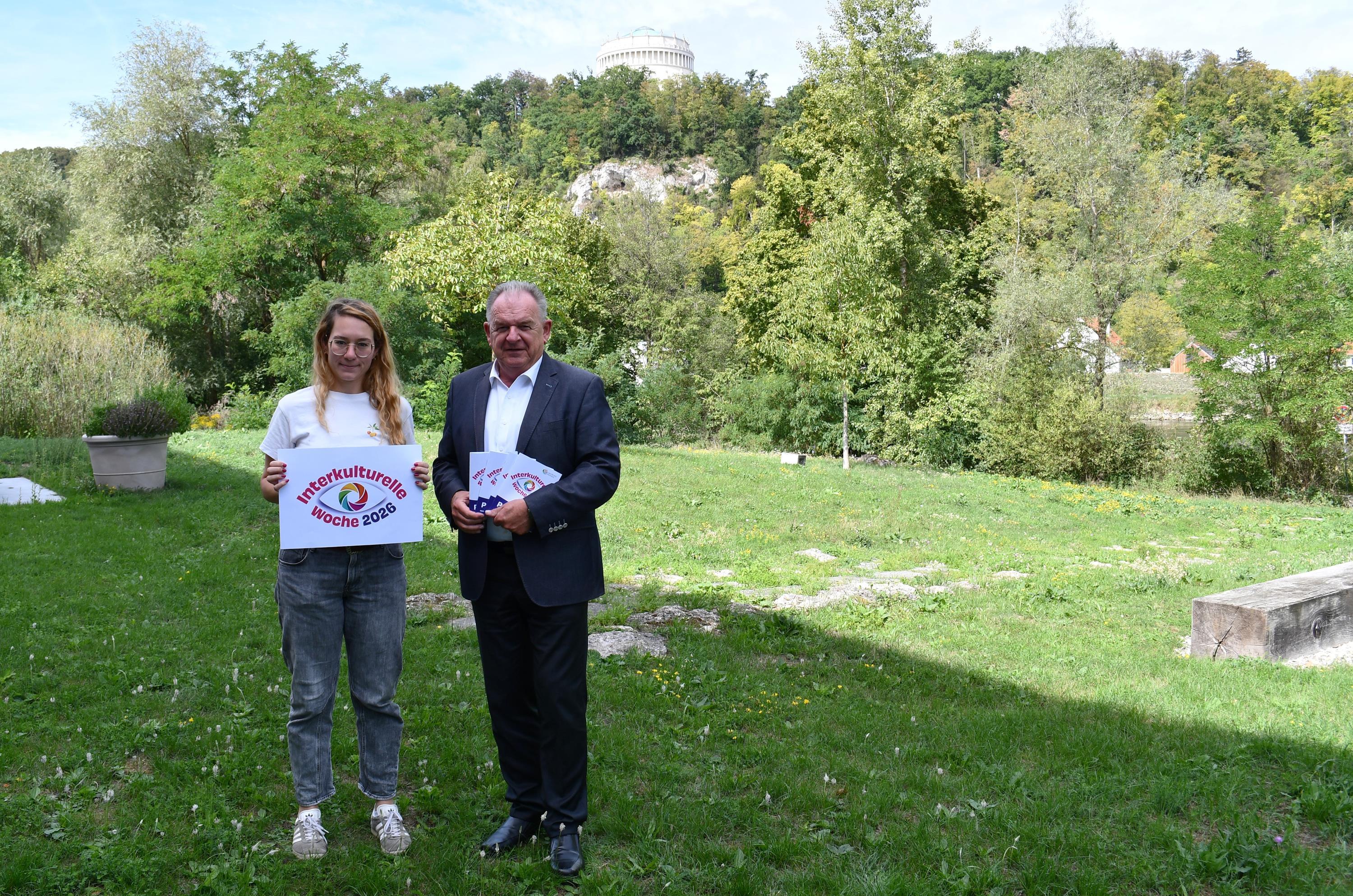 Frau und Mann mit Flyern stehen auf grüner Wiese neben Landratsamt