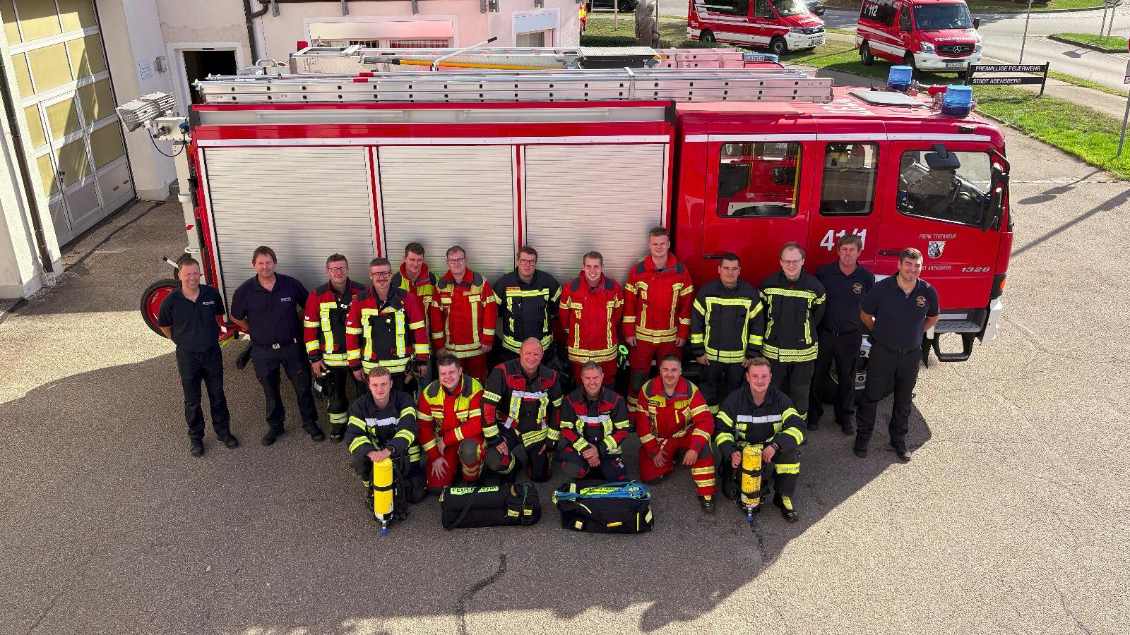 19 Feuerwehrmänner stehen neben einem Feuerwehrauto