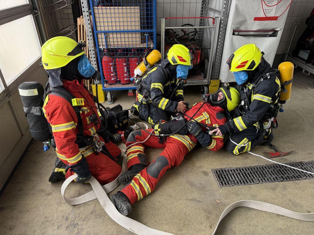 3 Feuerwehrmänner mit Atemschutzmasken kümmern sich um Feuerwehrmann