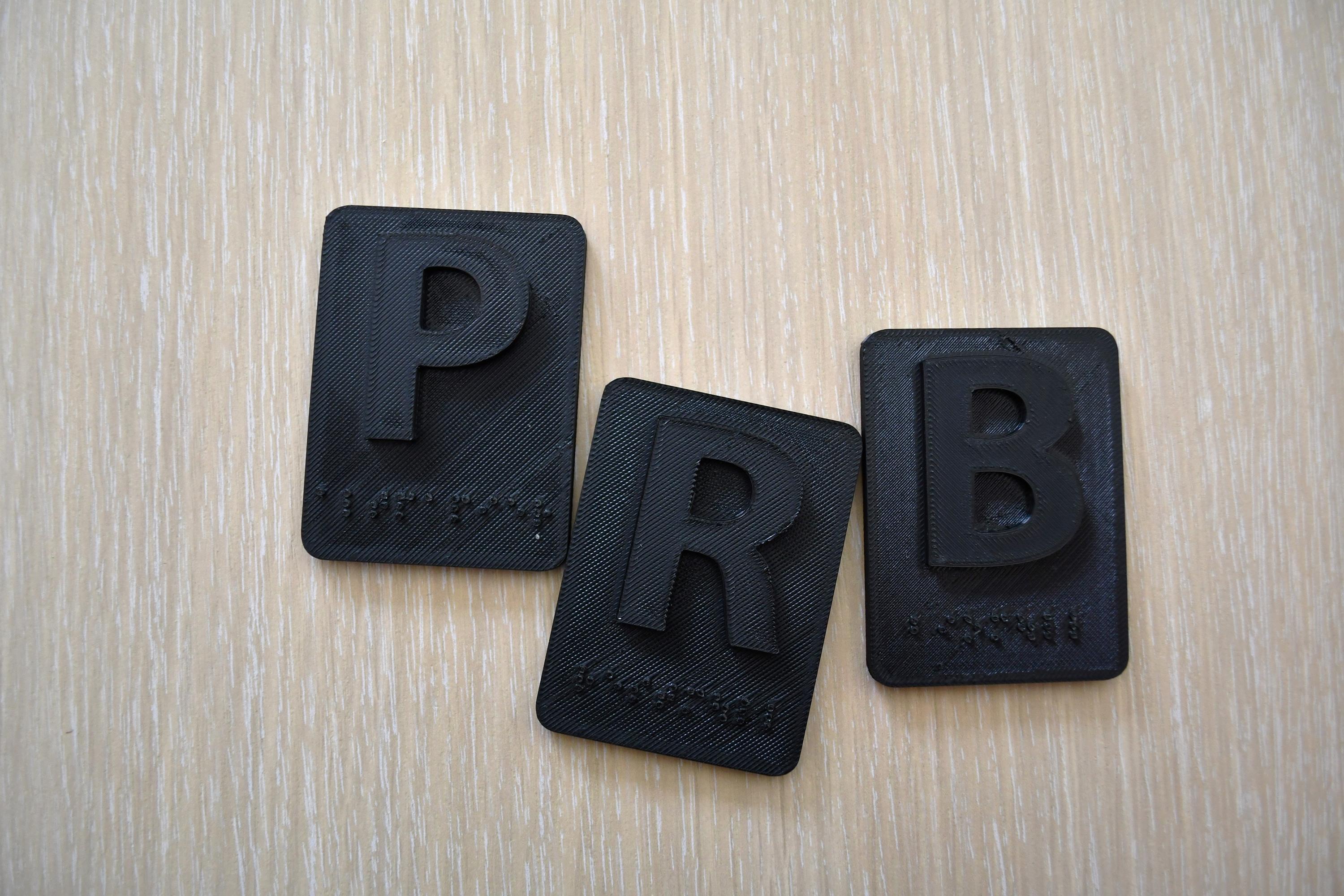 Drei schwarze Sticker mit den Buchstaben P, R und B auf Holztisch