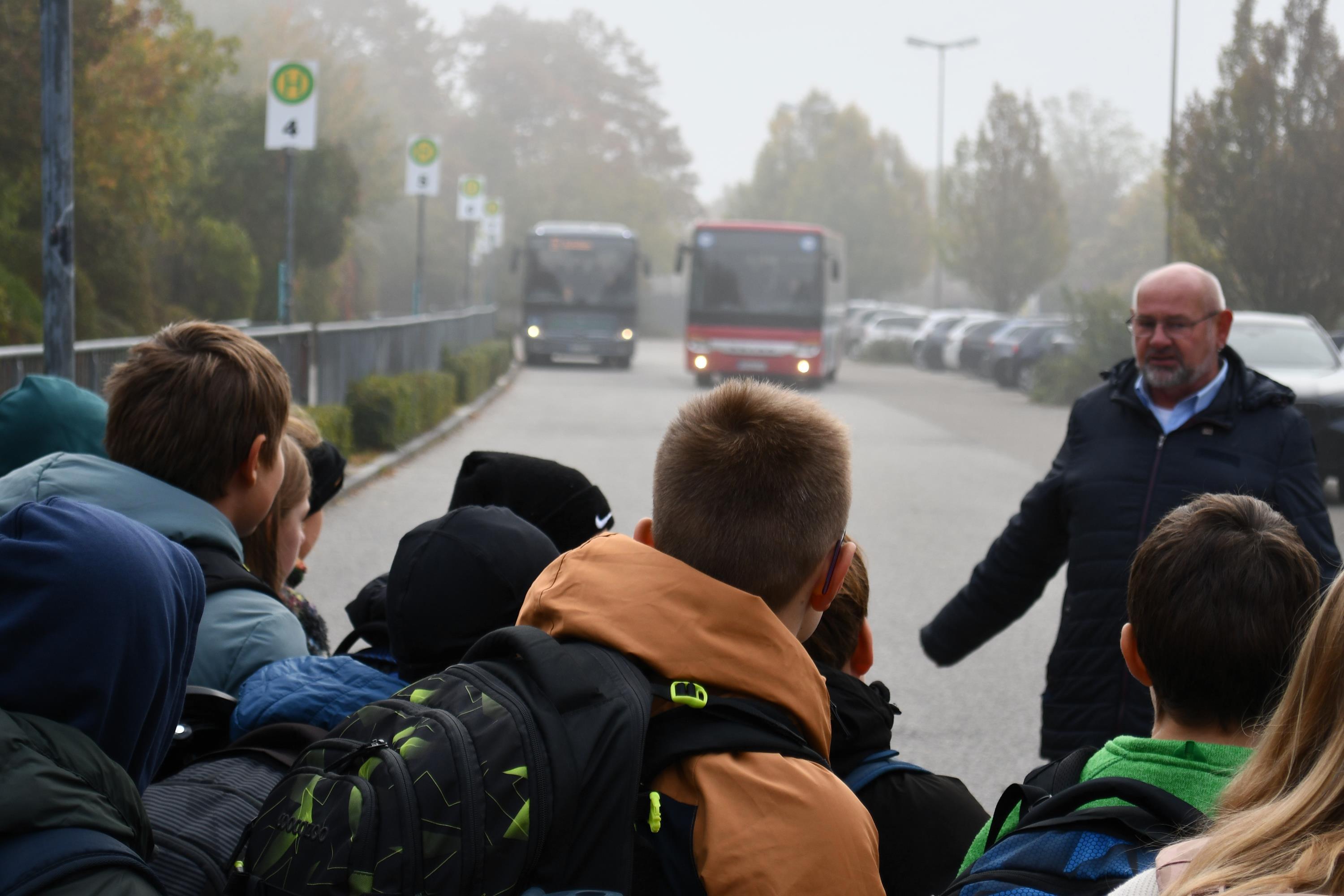 Schüler stehen am Fahrbahnrand und warten auf einen ankommenden Bus