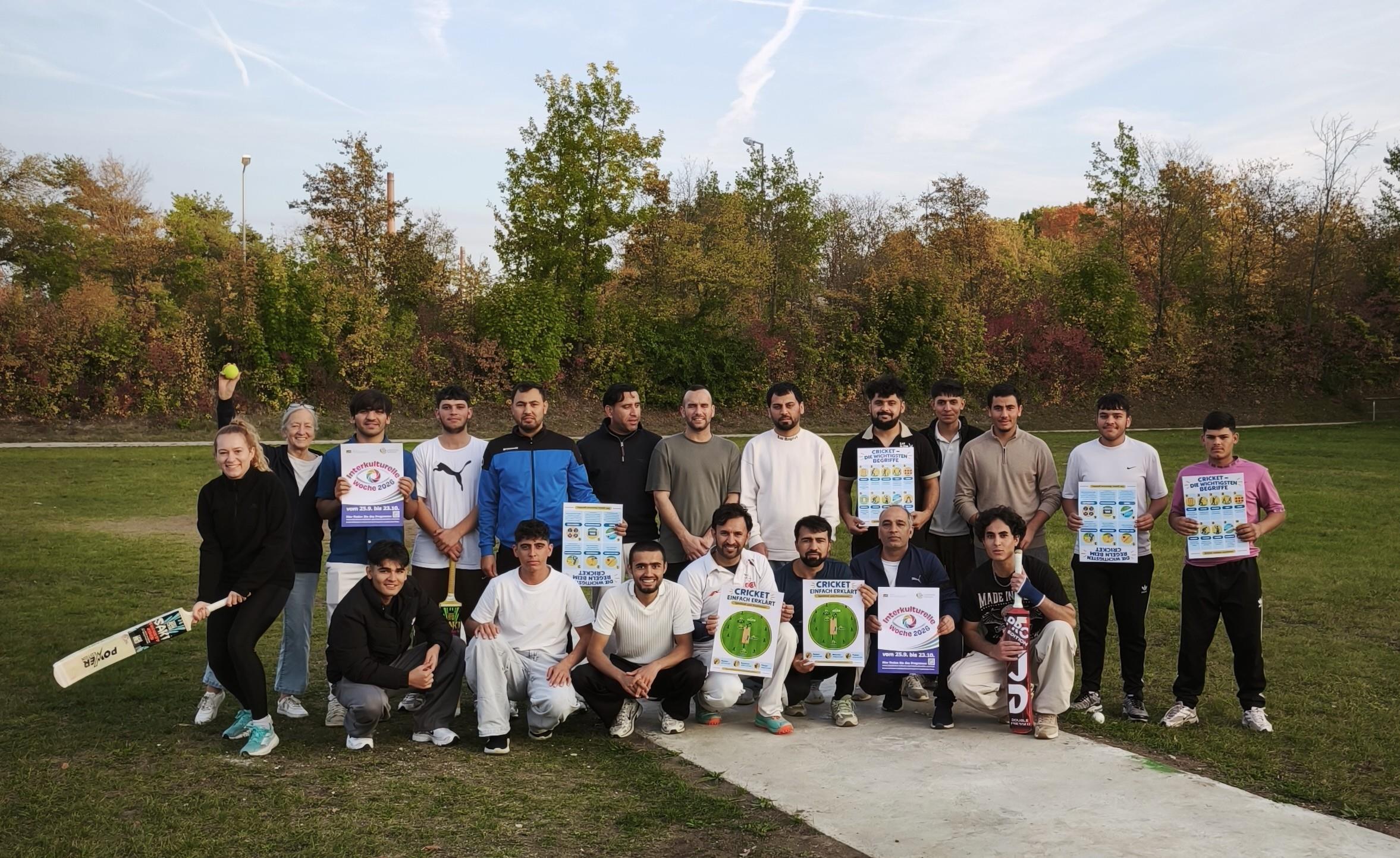 18 Männer und 2 Frauen mit Cricketschlägern und Plakaten auf Wiese
